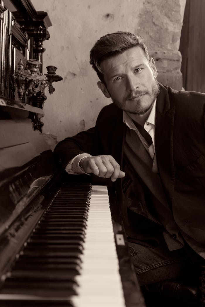 services-03 Sophisticated portrait of a man in a suit leaning against a piano with sepia tones.