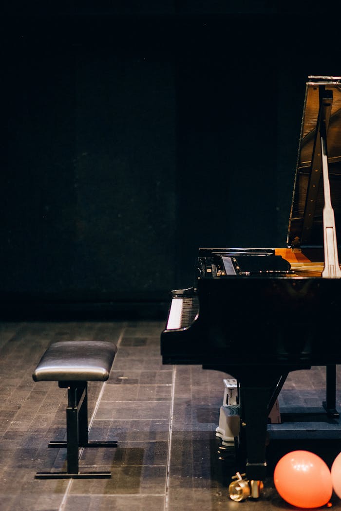 Stylish grand piano on stage, accompanied by a bench and colorful balloons, hinting at a musical event.